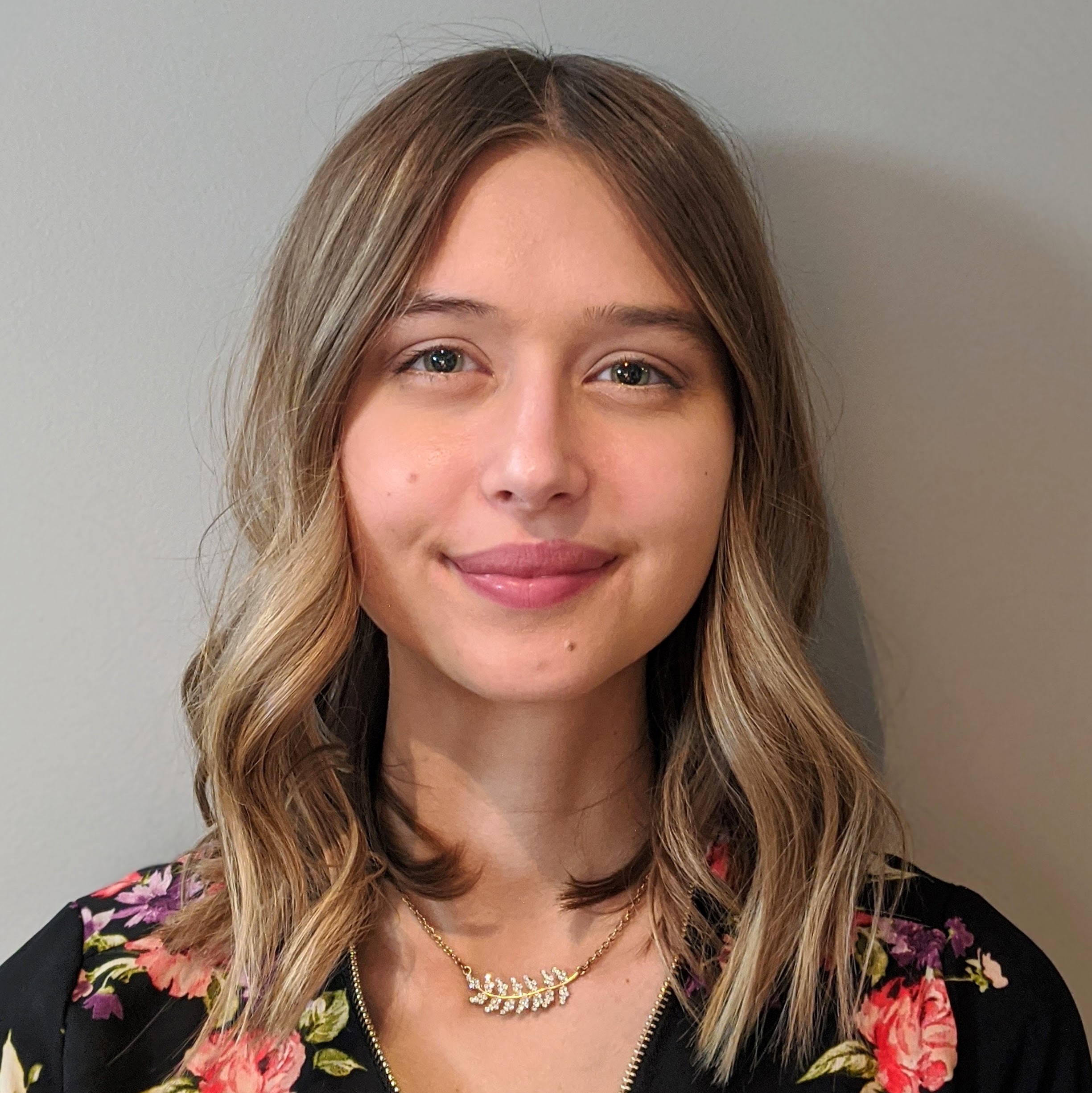 Headshot of Genna Weber, a young white female with culy hair wearing a floral shirt.